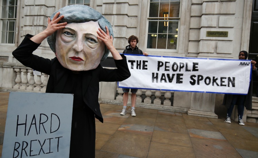 A demonstrator wears a mask depicting Britain's Prime Minister and leader of the Conservative Party Theresa May, poses with a mock gravestone bearing the words 
