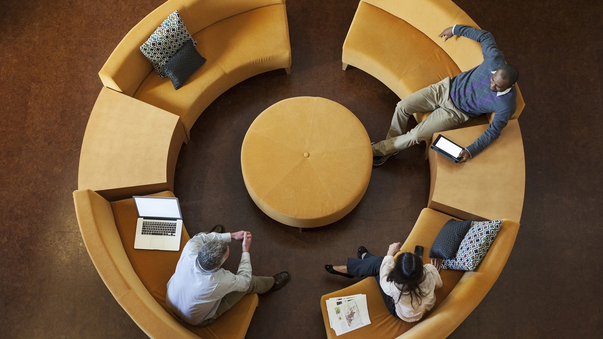 Overhead view of people sitting on a circular sofa, surrounded by devices