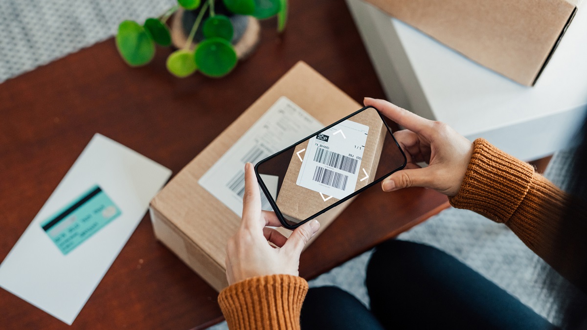Woman Scanning Delivery Barcode On Package With Smart Phone