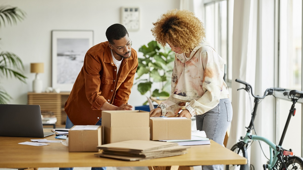 Male and female freelancers analyzing packaging at table. Businessman and businesswoman are working from home office. They are in living room.